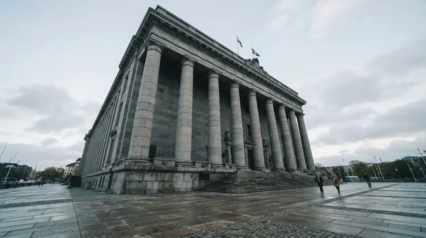 Rettsbygning i granitt sett nedenfra med høye søyler og en rolig plass foran, bleke skyer på himmelen